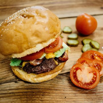 Szürkemarha burger, vörös cheddarral, mangalica szalonnával, karamellizált hagymával és fűszeres Agria burgonya hasábbal